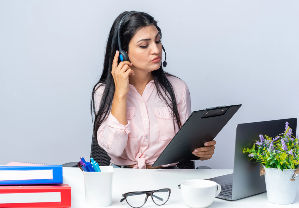 young-beautiful-woman-casual-clothes-with-headphones-microphone-holding-clipboard-looking-it-with-serious-face-sitting-table-with-laptop-white